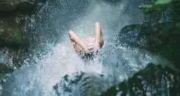 high-angle photography of woman bathing below waterfalls during daytime