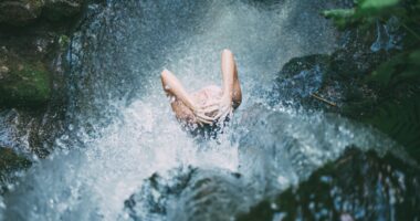 high-angle photography of woman bathing below waterfalls during daytime