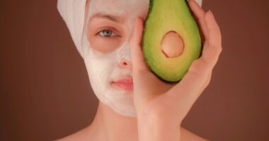woman with white face mask holding green fruit